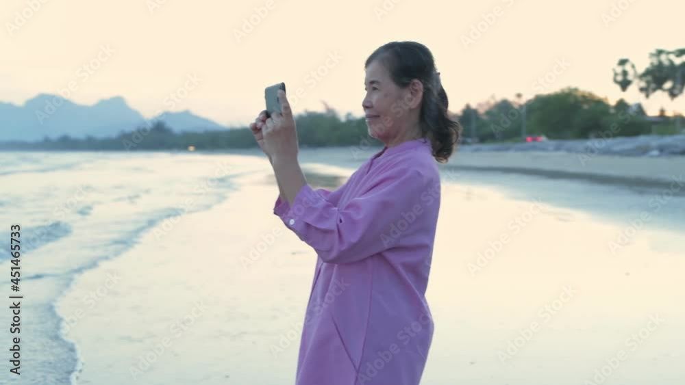 Holiday concept of 4k Resolution. An old Asian woman happily playing with a mobile phone on the beach. Holiday concept of 4k Resolution. An old Asian woman happily playing with a mobile phone on the beach.
