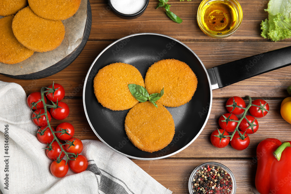 Delicious fried breaded cutlets, spices and vegetables on wooden table, flat lay