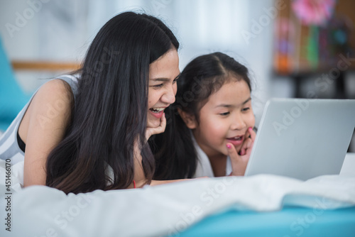 children and girl sisters having fun to watching online video on laptop computer cyberspace, childhood people family or young mother and little daughter are happy together at home with technology