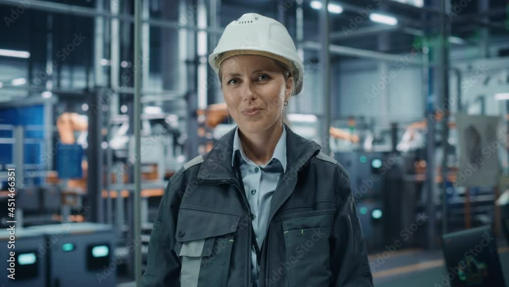 Car Factory Office: Portrait of Female Chief Engineer Wearing Hard Hat Looking at Camera, Smiling. Professional Technician. Automated Robot Arm Assembly Line Manufacturing High-Tech Electric Vehicles Car Factory Office: Portrait of Female Chief Engineer Wearing Hard Hat Looking at Camera, Smiling. Professional Technician. Automated Robot Arm Assembly Line Manufacturing High-Tech Electric Vehicles