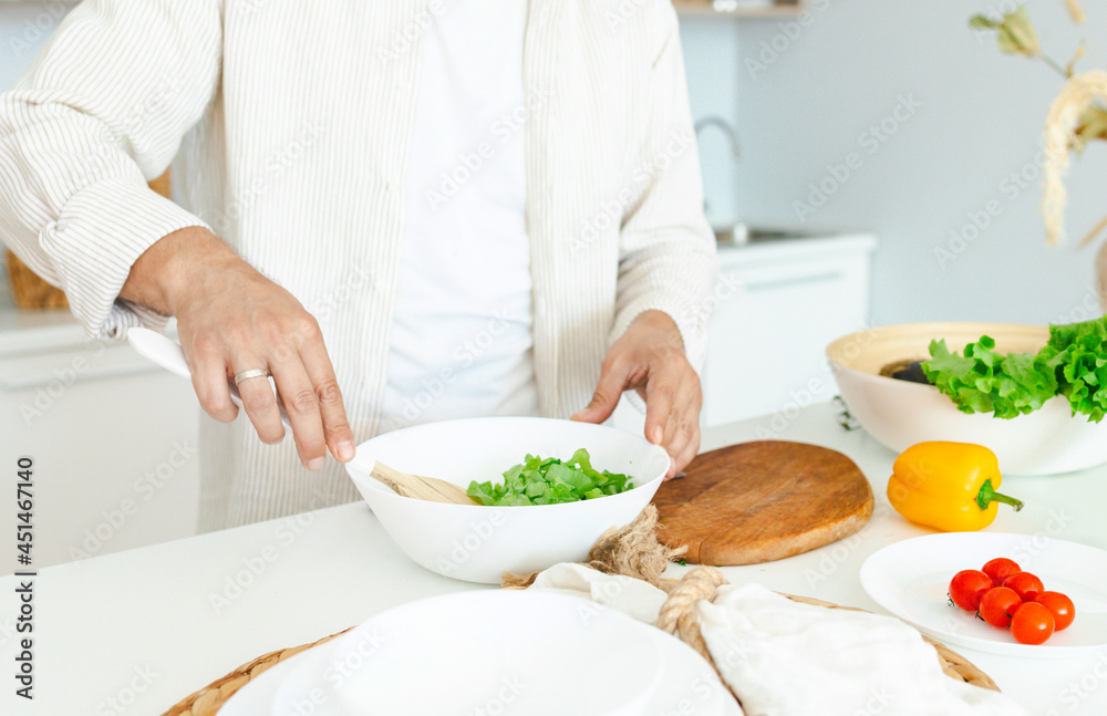 happy young, handsome, bearded man is standing in the modern kitchen prepares a salad of fresh vegetables, cuts vegetables with a knife on a cutting board, cooking as concept of a man's hobby