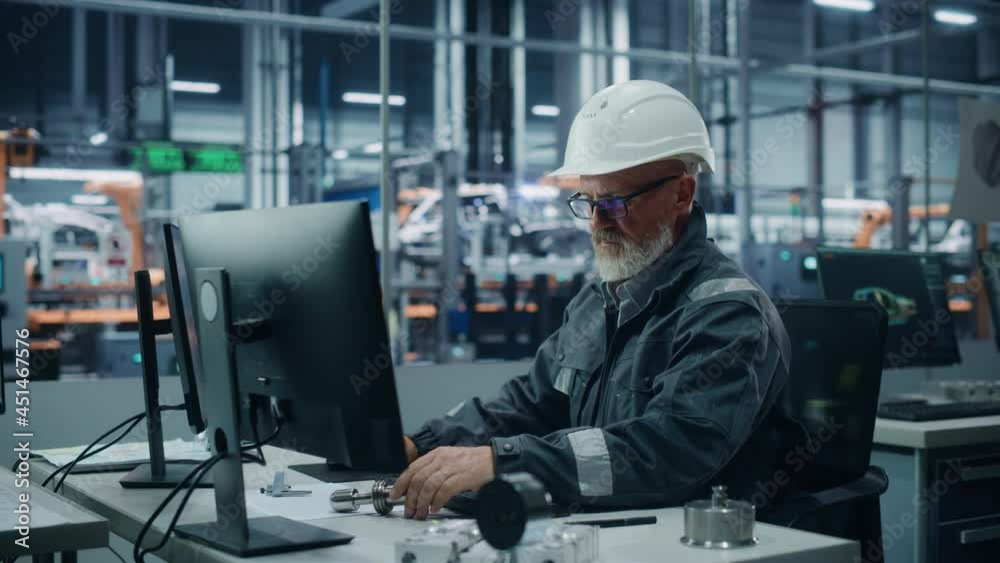 Car Factory Office: Portrait of Male Engineer Wearing Safety Hard Hat Working on Computer. Techniciancian Constructing Component. Automated Robot Arm Assembly Line Manufacturing Electric Vehicles Car Factory Office: Portrait of Male Engineer Wearing Safety Hard Hat Working on Computer. Techniciancian Constructing Component. Automated Robot Arm Assembly Line Manufacturing Electric Vehicles