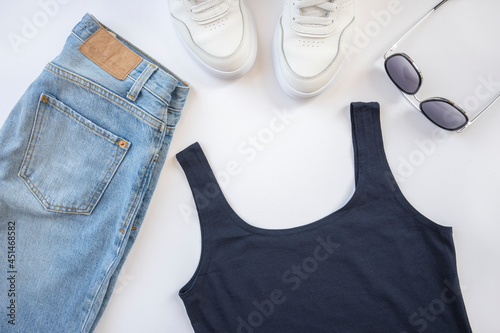 Casual outfit. Jeans, top, sunglasses and white sneakers lie on a white background