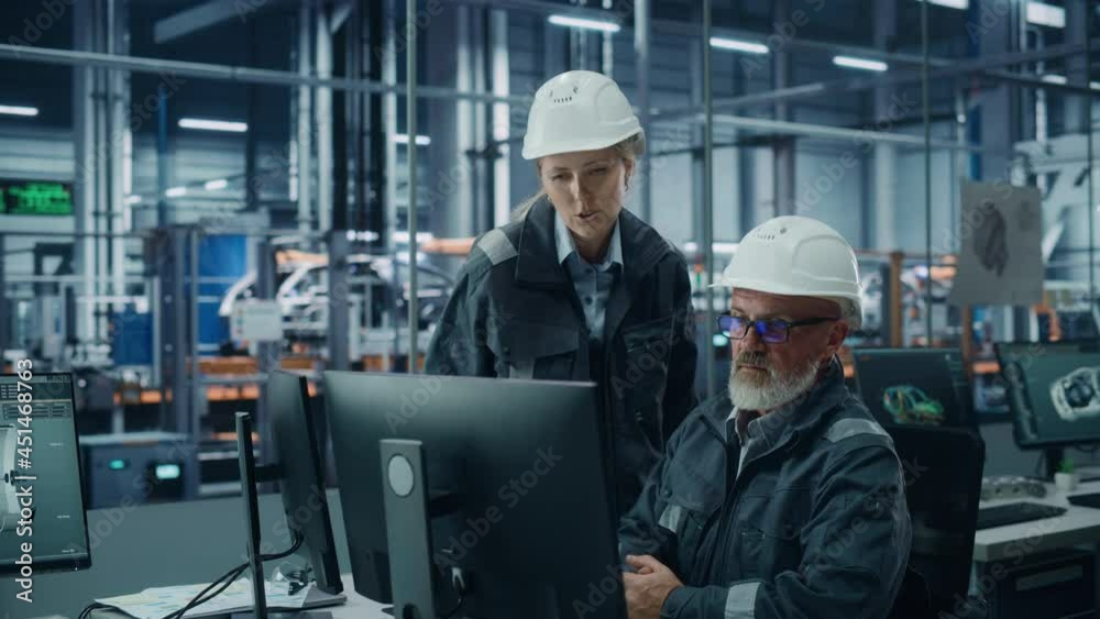 Car Factory Office: Female Manager Talks to Male Automotive Engineer Working on Computer. Automated Robot Arm Assembly Line Manufacturing Electric Vehicles. Technicians Monitoring Conveyor Production Car Factory Office: Female Manager Talks to Male Automotive Engineer Working on Computer. Automated Robot Arm Assembly Line Manufacturing Electric Vehicles. Technicians Monitoring Conveyor Production