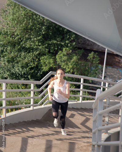 A woman runs up the stairs of the bridge. Evening training in the city.