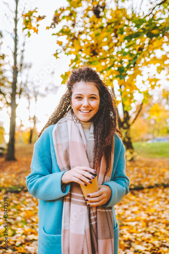 Happy attractive afro-haired woman walk in autumn park at sunny warm day with cup of coffee