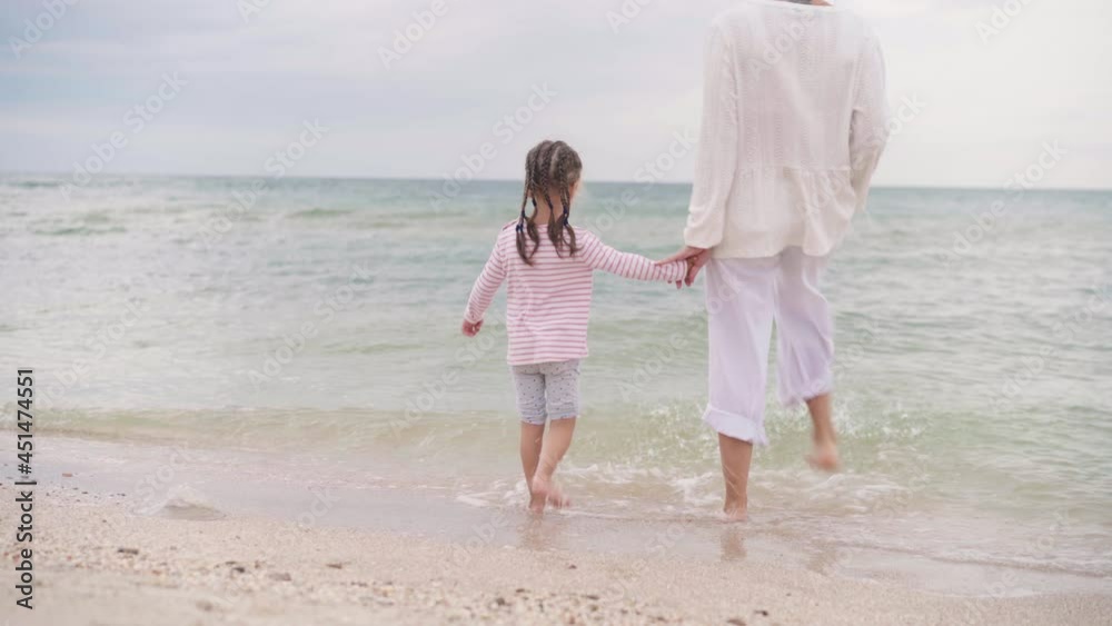 Mother With Little Daughter Walking Along the Sea Happy Family on the Beach Mother holds hand little child walking along the seashore. Traveling Summer Vacation Concept Mother With Little Daughter Walking Along the Sea Happy Family on the Beach Mother holds hand little child walking along the seashore. Traveling Summer Vacation Concept