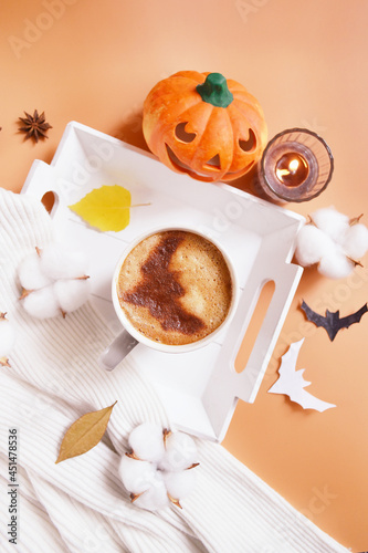 Halloween celebration coffee on the tray with smiling pumpkin, candle, coconut flowers and bats on the orange background. Halloween service. Trick or Treat! Eat, drink, and be scary. Happy Howloween.  photo