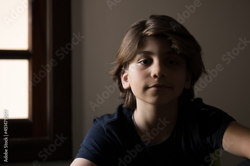 retrato de garoto de 10 anos com cabelo comprido e com o rosto iluminado apenas do seu lado direito  photo