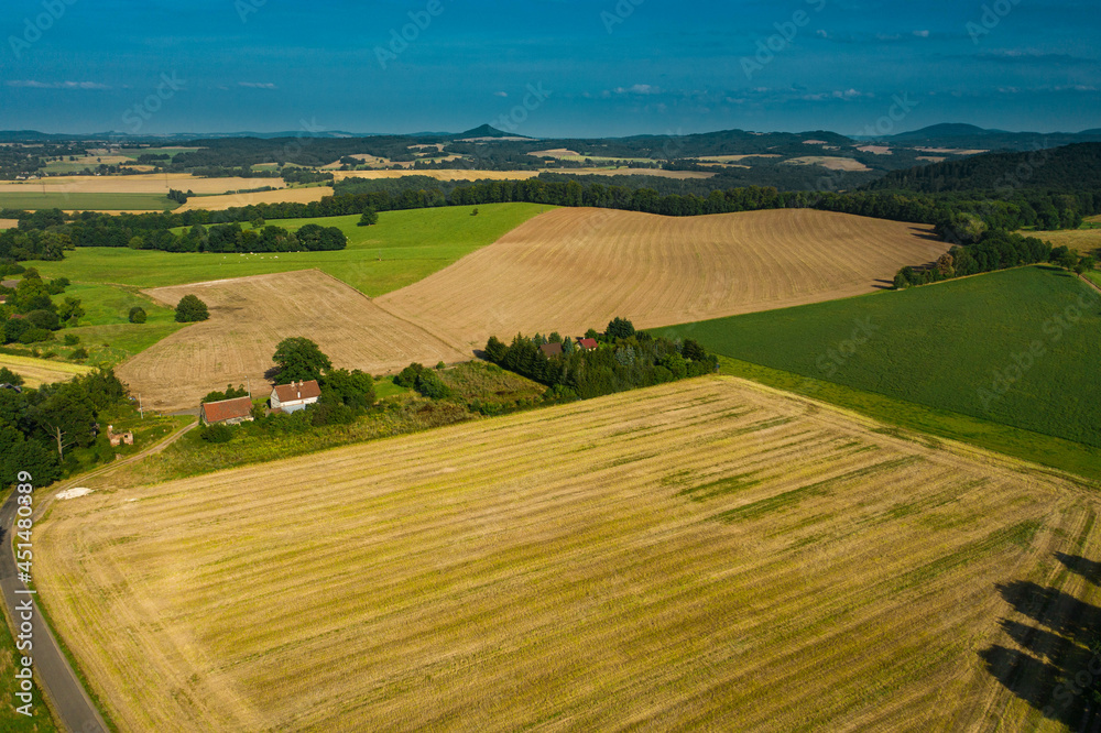 Sudeten foothills. Undulating terrain covered with arable fields, meadows, clumps of trees. In the distance you can see the buildings of the village and mountains on the horizon. Photo from the drone.
