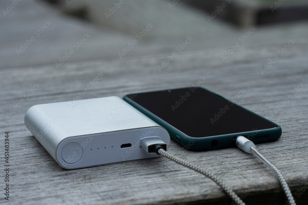 Power Bank charges a smartphone on a wooden bench in the park. Power Bank charges a smartphone on a wooden bench in the park.