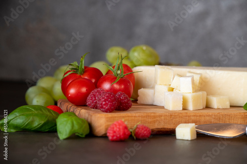 tomatoes, cheese, basil, raspberries and grapes on an olive board on a dark background