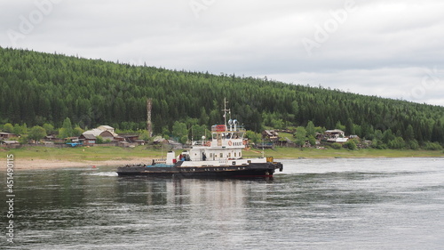 View of Lena river in Ust-Kut city, Siberia. A tugboat ship Nakat owned by Rosmorrechflot, with rural houses in background