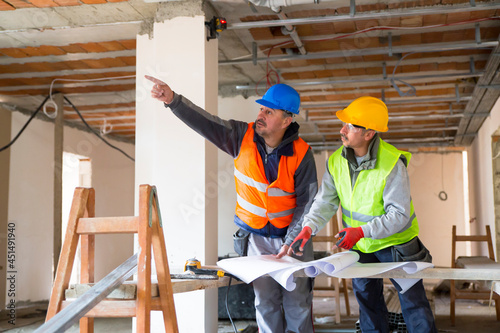 Mature construction workers with blueprints on construction site
