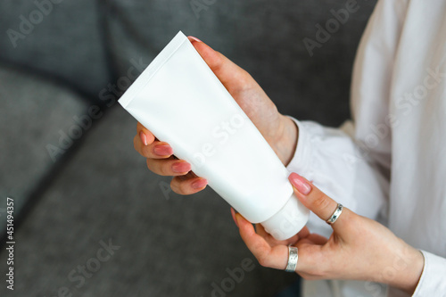 Woman hand holding a white tube with cream