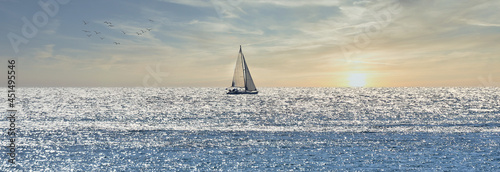 Photography Small sailboat sailing through a silver sea at sunrise