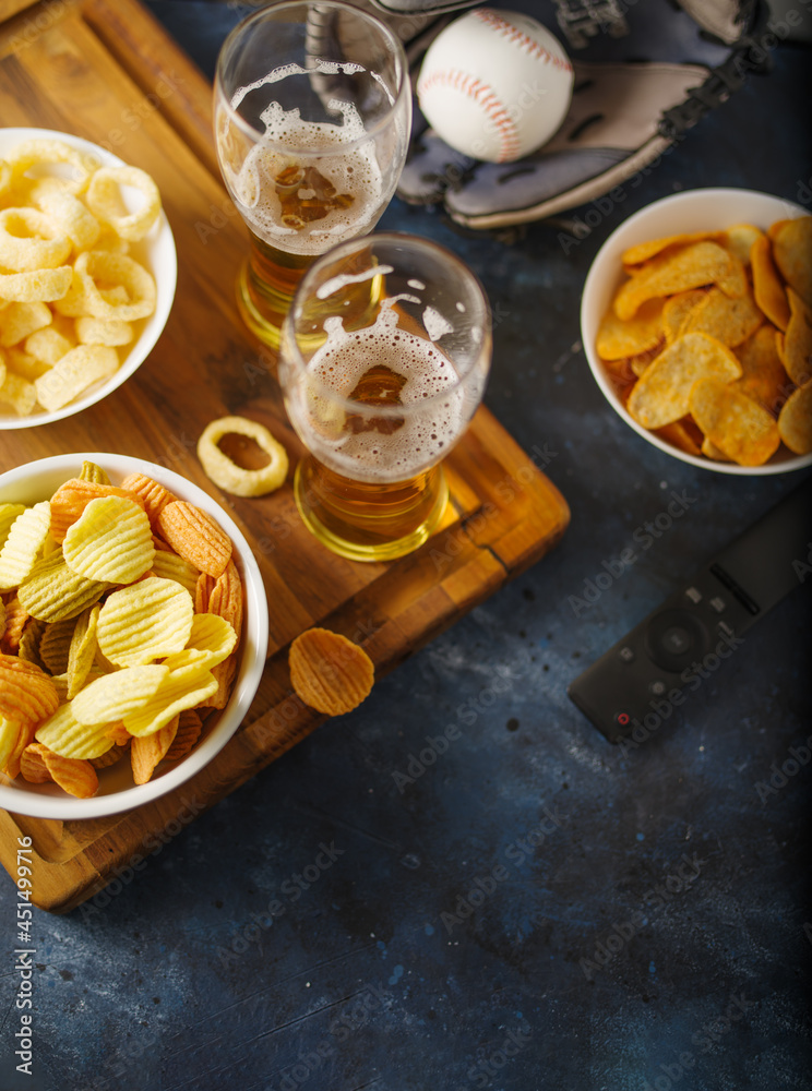 Beer in glasses and snacks - chips, onion rings, remote control. In the background is a baseball glove. Sports fans, group of friends, family, leisure. Watching sports matches on TV. Beer in glasses and snacks - chips, onion rings, remote control. In the background is a baseball glove. Sports fans, group of friends, family, leisure. Watching sports matches on TV.