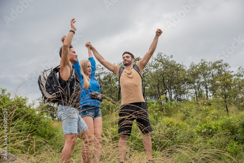 Two handsome men and womn raising their hands while standing on a rock during a trekking trip, feeling free