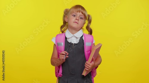 Smiling funny schoolgirl wears backpack, making humorous face with eyes crossed, playing fool, having fun with stupid brainless dumb expression over yellow studio background. Back to school concept
