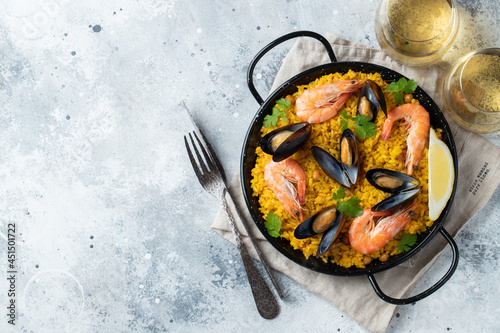 Traditional spanish seafood paella in pan with chickpeas, shrimps, mussels, squid on light grey concrete background. Top view with copy space