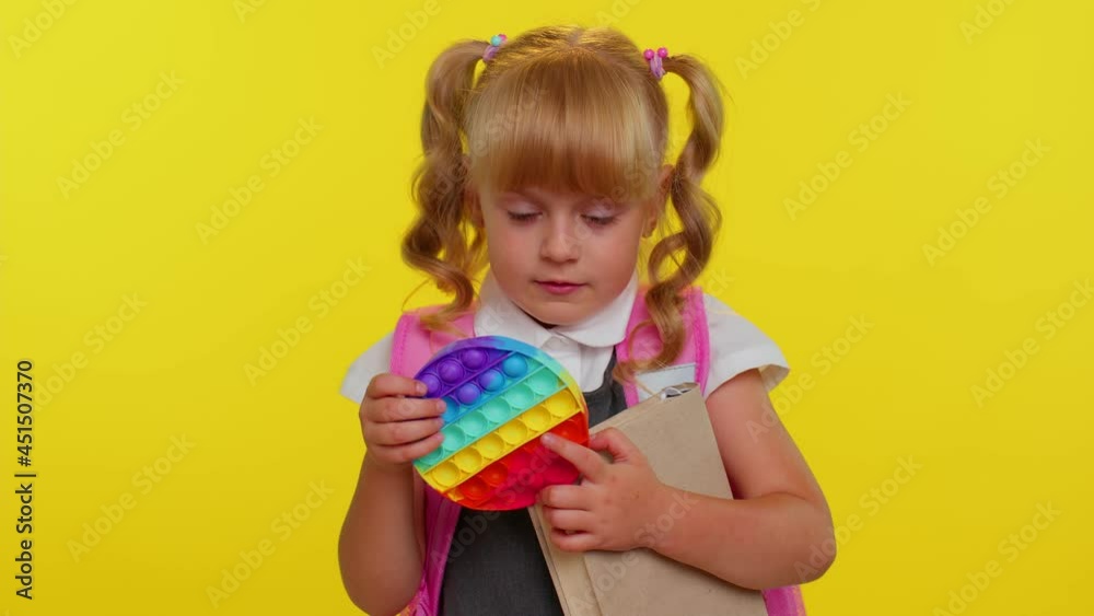 Funny pupil girl playing with pop it sensory anti-stress toy. Kid presses on colorful squishy bubbles. Stress and anxiety relief. Yellow studio background. Trendy fidgeting game for stressed children Funny pupil girl playing with pop it sensory anti-stress toy. Kid presses on colorful squishy bubbles. Stress and anxiety relief. Yellow studio background. Trendy fidgeting game for stressed children