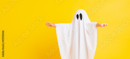 Funny Halloween Kid Concept, Closeup a little cute child with white dressed costume halloween ghost scary, studio shot isolated on yellow background