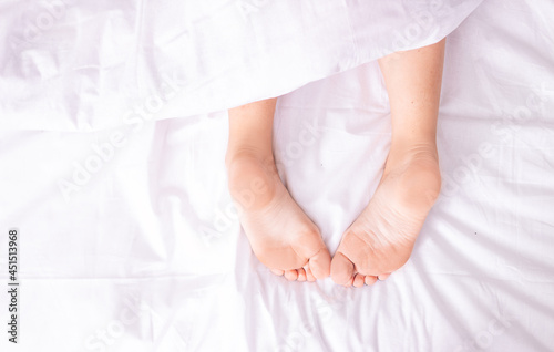 Bare feet, a girl sleeping on the bed and covered with a white blanket on a bright Sunday morning.