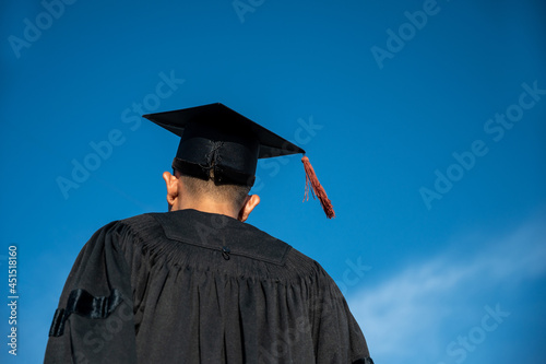 Rear View Of man In Graduation Gown Holding cap Standing Against Sky photo