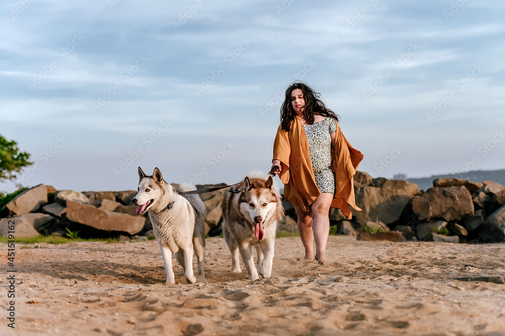 one girl walking with two husky dogs at the beach