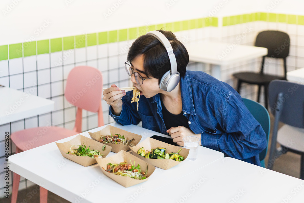 Young man wearing headphone is concentrating on eating cold dishes