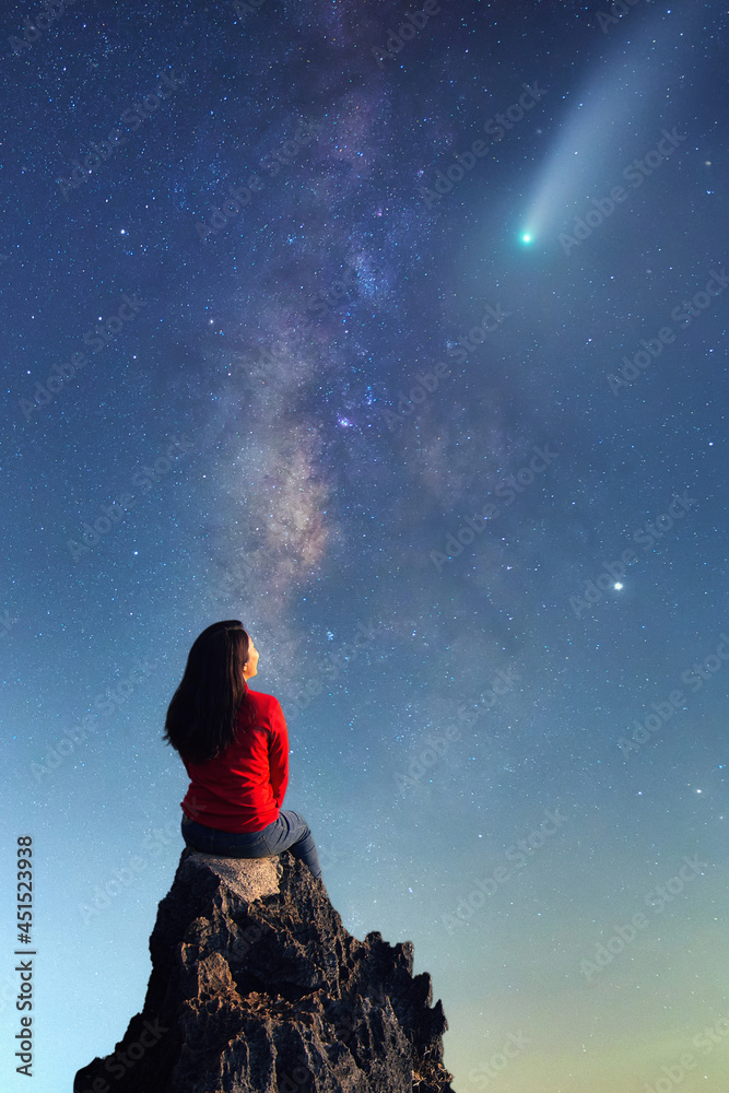 A young woman watching the beauty of the Milky Way and a meteor on the rocks.