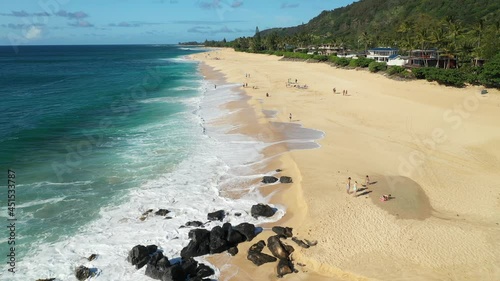 Wallpaper Mural Aerial drone footage above a beach on Oahu, Hawaii, USA. Broad, sandy beach with turquoise water and white waves, and sunbathers visible on the sand. Green forest to the right of the beach. Torontodigital.ca