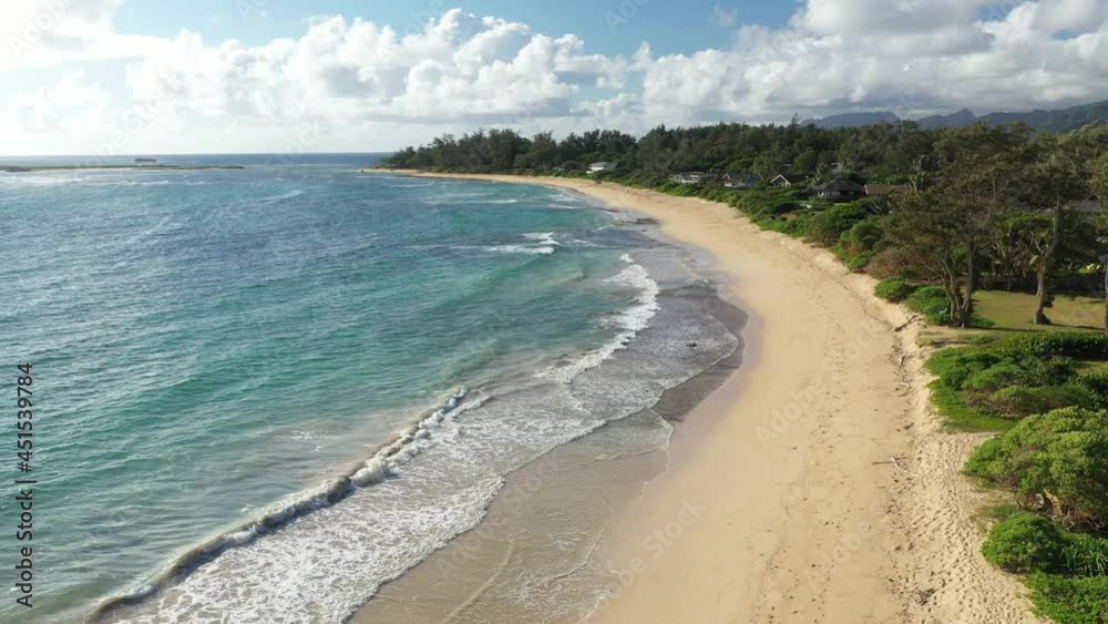 Aerial drone view of Malaekahana Beach on the island of Oahu, Hawaii. No people on beach, white sand in a crescent shape with green forest and partly cloudy blue sky in the background. Aerial drone view of Malaekahana Beach on the island of Oahu, Hawaii. No people on beach, white sand in a crescent shape with green forest and partly cloudy blue sky in the background.