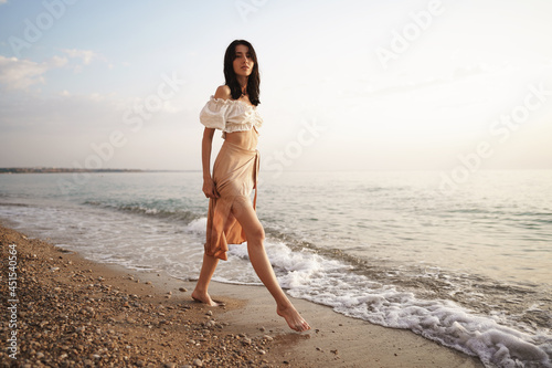 Lonely young woman walks on the seashore at sunset