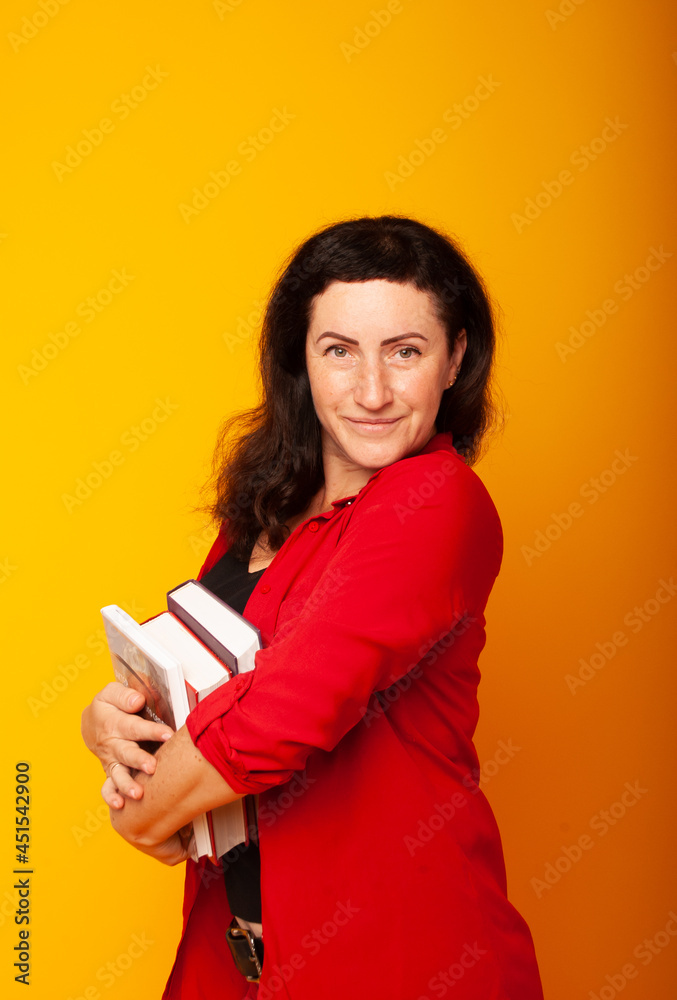 woman on a yellow background with books in her hands, posing on an isolated background. Business woman in red suit in a dreamy, joyful mood woman on a yellow background with books in her hands, posing on an isolated background. Business woman in red suit in a dreamy, joyful mood