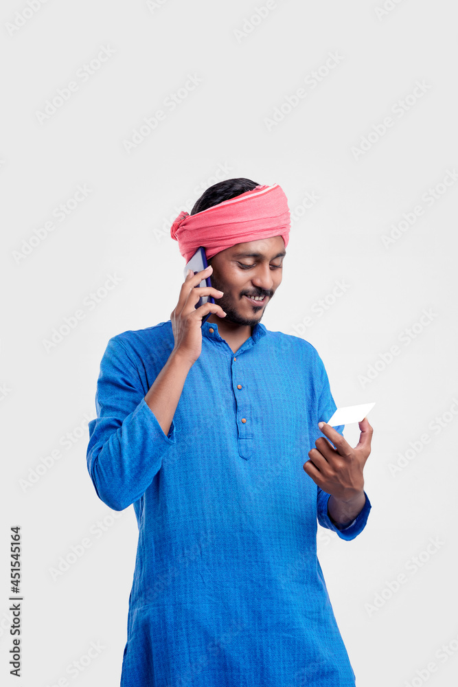 Naklejka premium Young indian man in traditional wear and talking on smartphone and using card over white background.