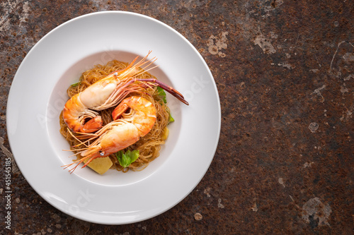 baked prawns with vermicelli, casseroled shrimps with glass noodles in white simply ceramic plate on rusty texture background with copy space, top view, river prawn