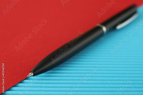 Black ballpoint pen lies on red blue background