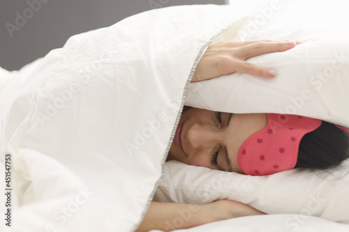 Woman lies in bed covering head with blanket closeup photo