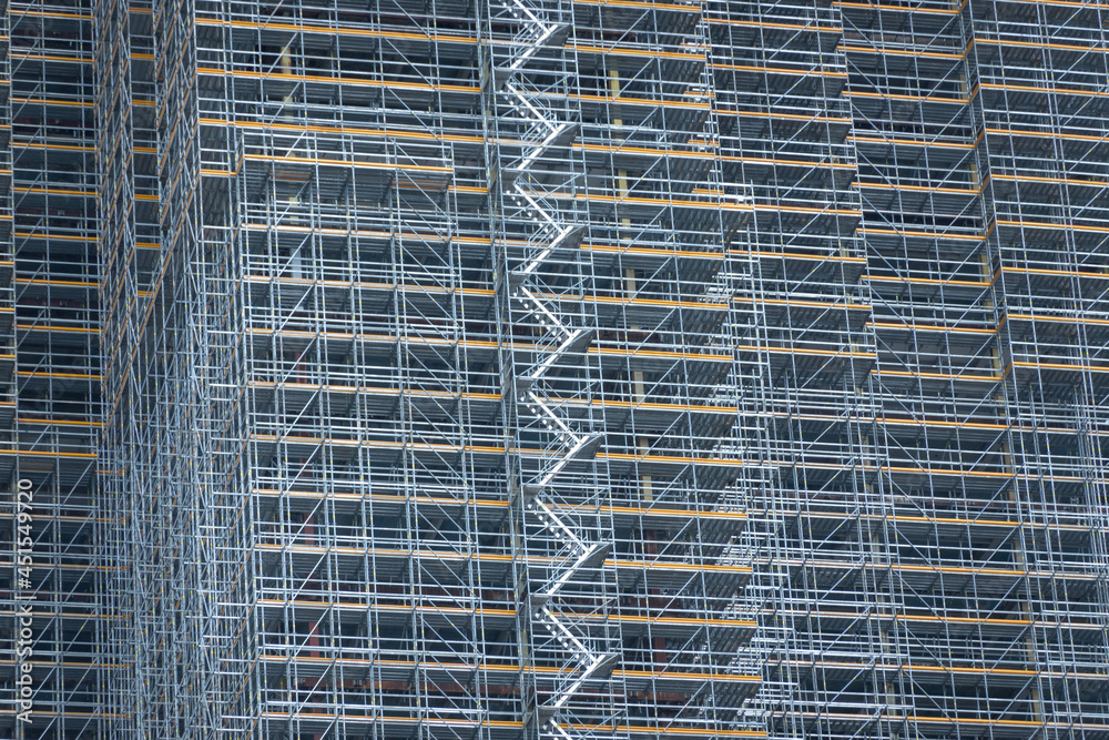 Scaffolding and metallic equipment around a high-rise building construction. No people, day light, outdoors.