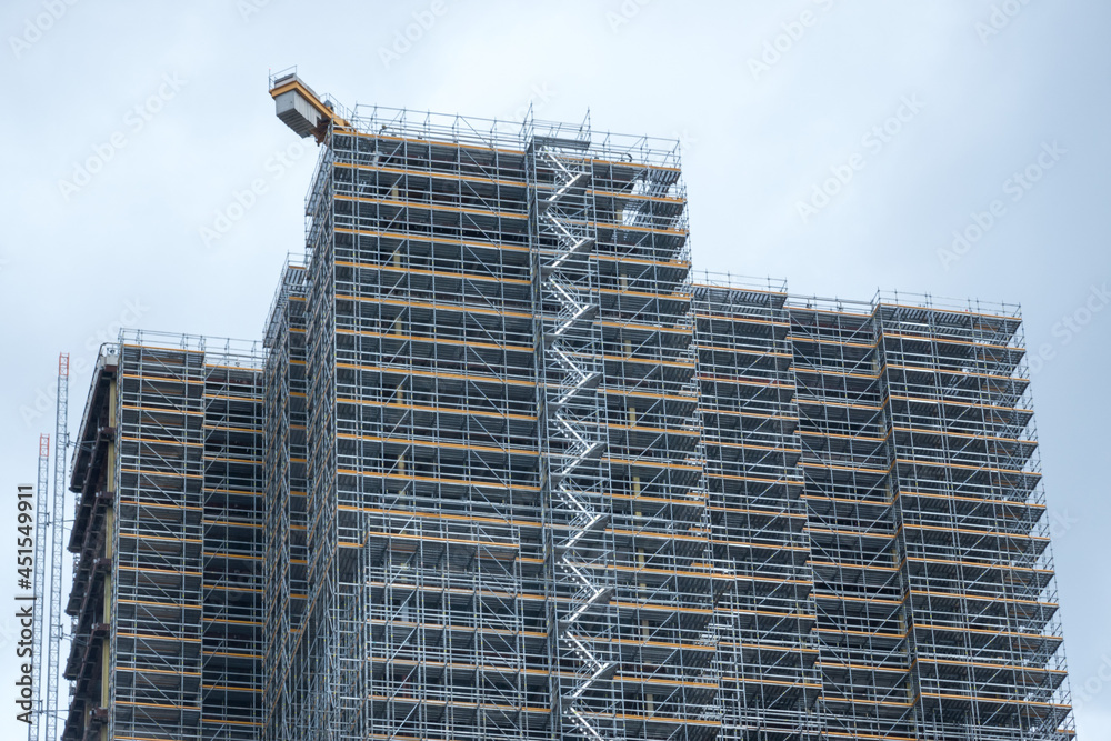 Fototapeta premium Scaffolding and metallic equipment around a high-rise building construction. No people, day light, outdoors.