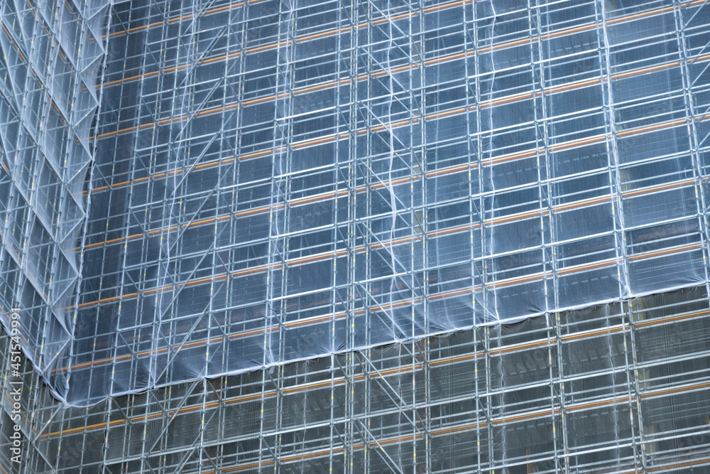 Scaffolding and metallic equipment around a high-rise building construction. No people, day light, outdoors.