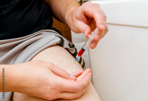 Close up view of man person do the B12 vitamin injection shot in home itself to himself in leg( vastus lateralis muscle) due to B12 deficiency what body do not absorb orally and do not produce. photo