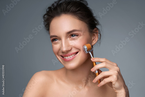Beautiful woman using derma roller for her facial skin. Photo of woman on gray background. Beauty and skin care concept photo