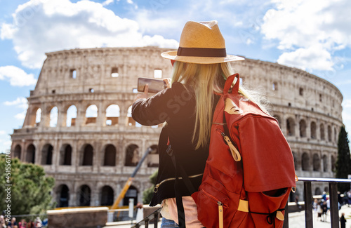 Photography Back view of young woman with red backpack and hat  which she's take a picture by smartphone at Colosseum in Rome, Italy
