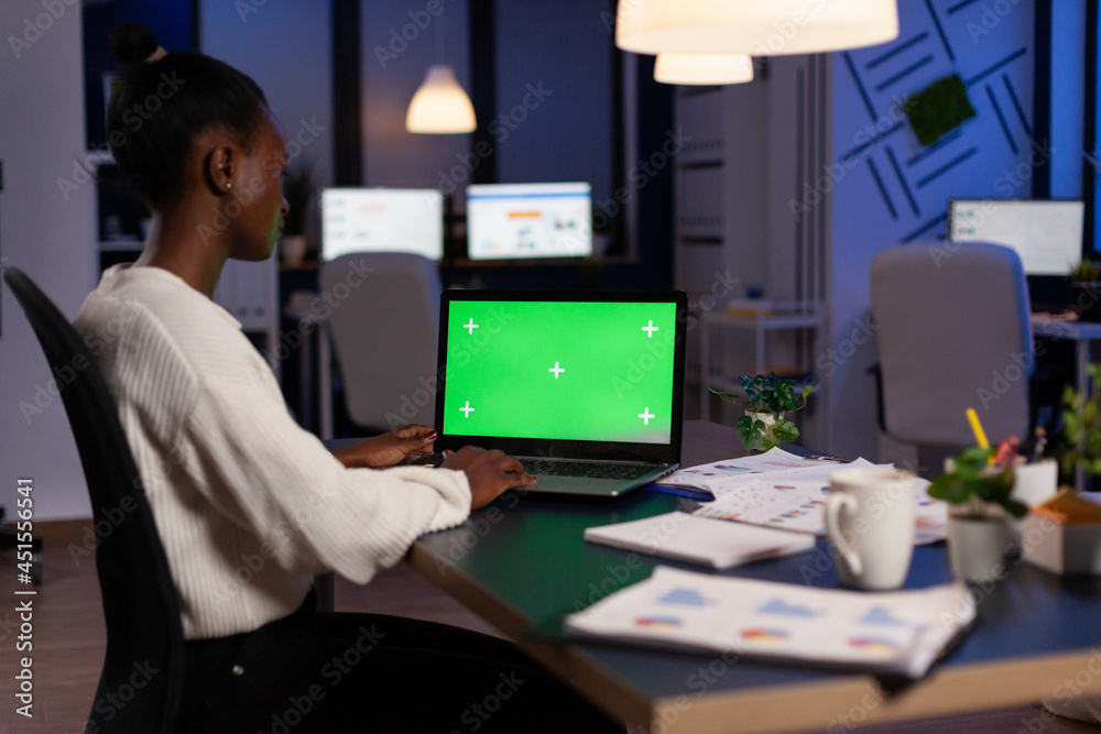 Concentrated african american businesswoman hardworking at financial strategy late at night in startup company office. Mock up green screen chroma key laptop with isolated display standing on table