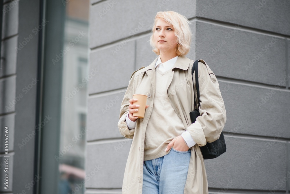 Fototapeta premium Cheerful stylish young woman in the street drinking morning coffee in sunshine light.