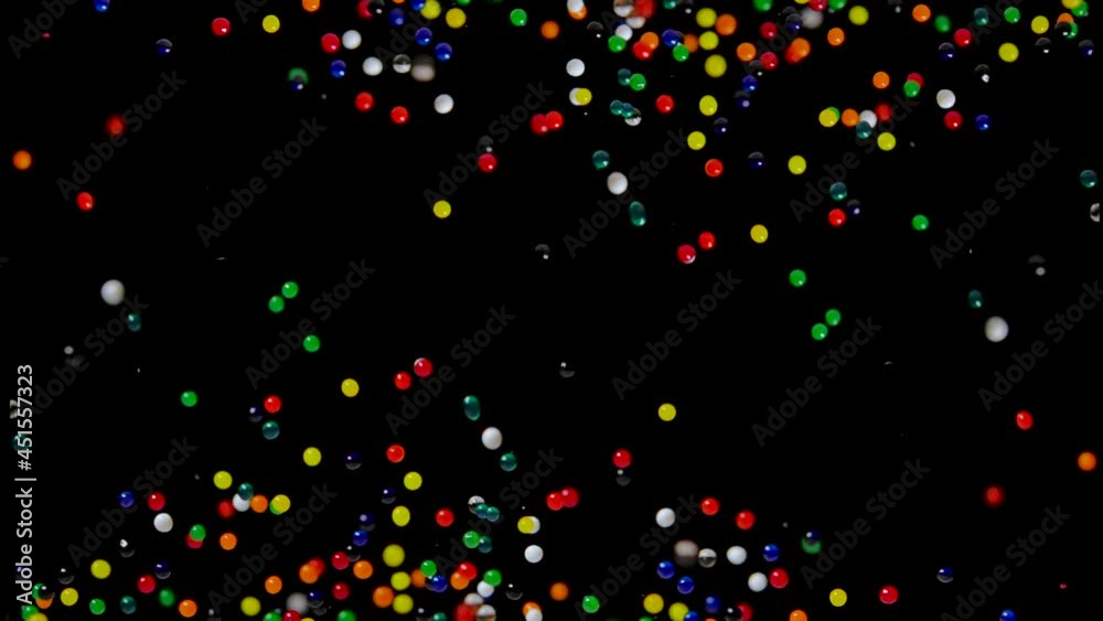 Many multicolored water gel balls move abstractly across the screen against a black background. Hydrogel balls orbeez bouncing and fly in different directions. Polymer superabsorbing gel. Close up