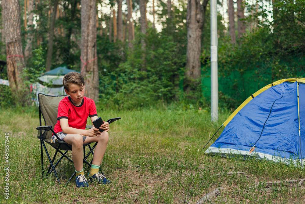 boy sitting in a folding chair and holding a smartphone against the background of summer nature boy sitting in a folding chair and holding a smartphone against the background of summer nature