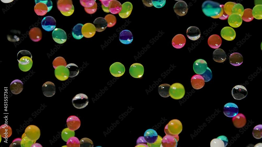 Many multicolored water gel balls move abstractly across the screen against a black background. Hydrogel balls orbeez bouncing and fly in different directions. Polymer superabsorbing gel. Close up